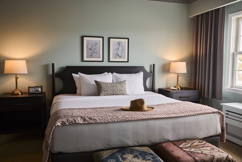 A king bed with a straw hat on the foot of the bed.