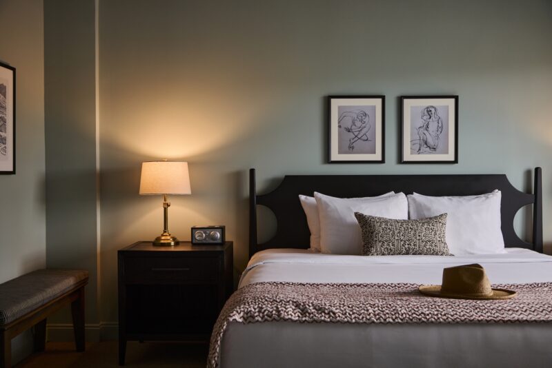 A king bed with a straw hat on the foot of the bed.