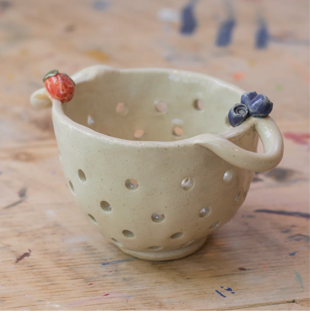 A cream ceramic berry bowl with a strawberry and blueberries on it.