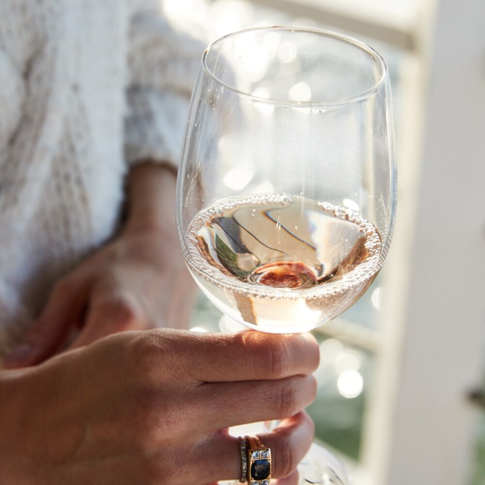 A woman holding a glass of rosé wine on a patio.
