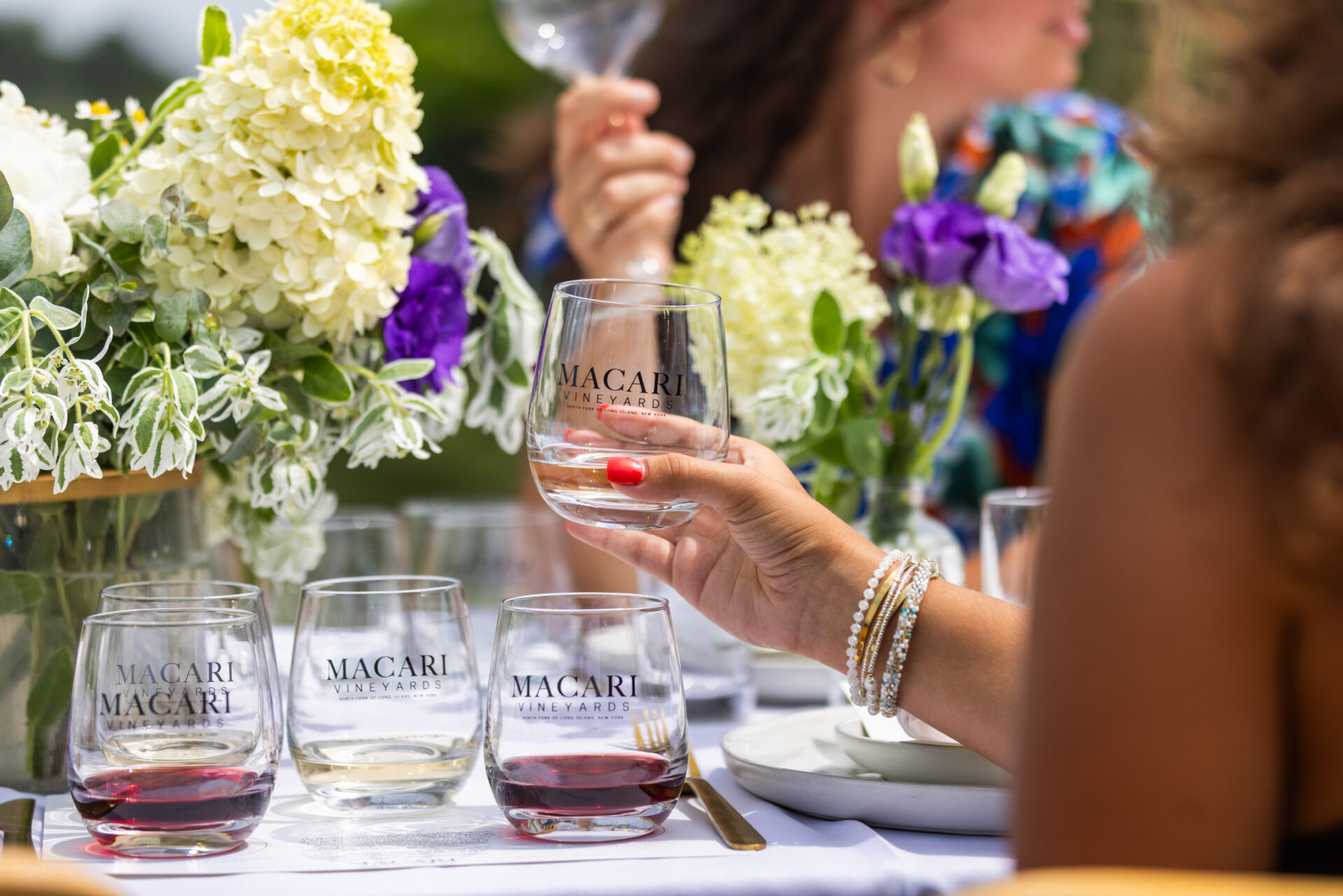 A woman holding wine glasses at a tasting at Macari Vineyard.