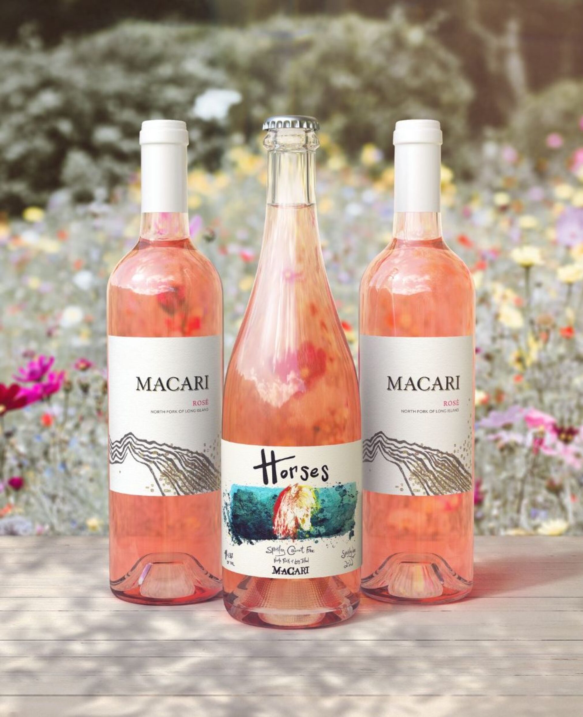 Three bottles of rosé wine next to flowers.