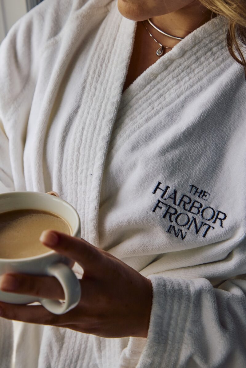 A woman in a Harbor Front Inn bathrobe holding a cup of coffee.