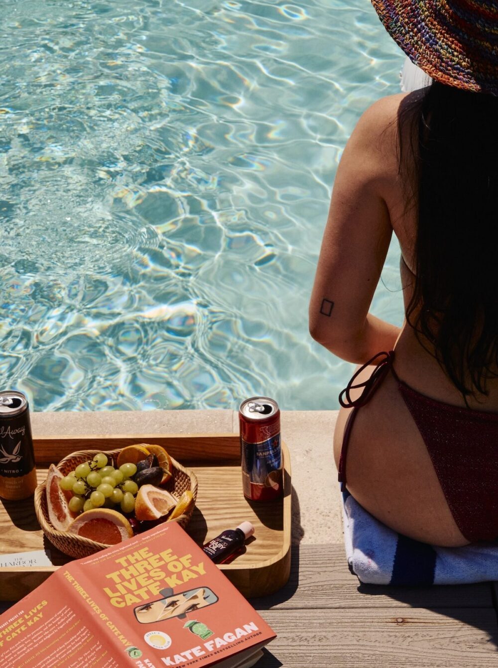 A woman sitting at the pool edge, enjoying snacks.
