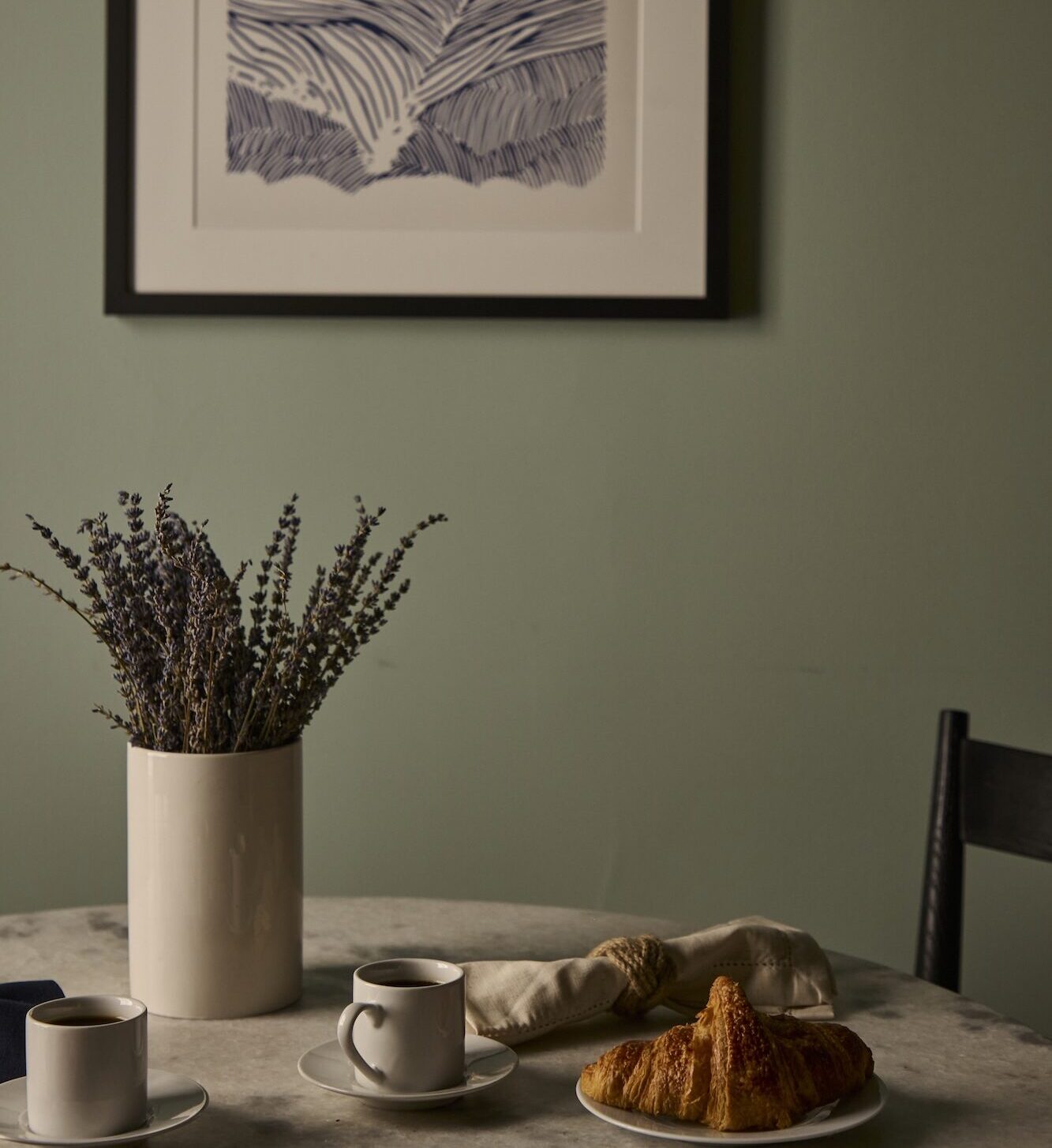 A bistro table with a vase of lavender, cups of coffee and pastries.