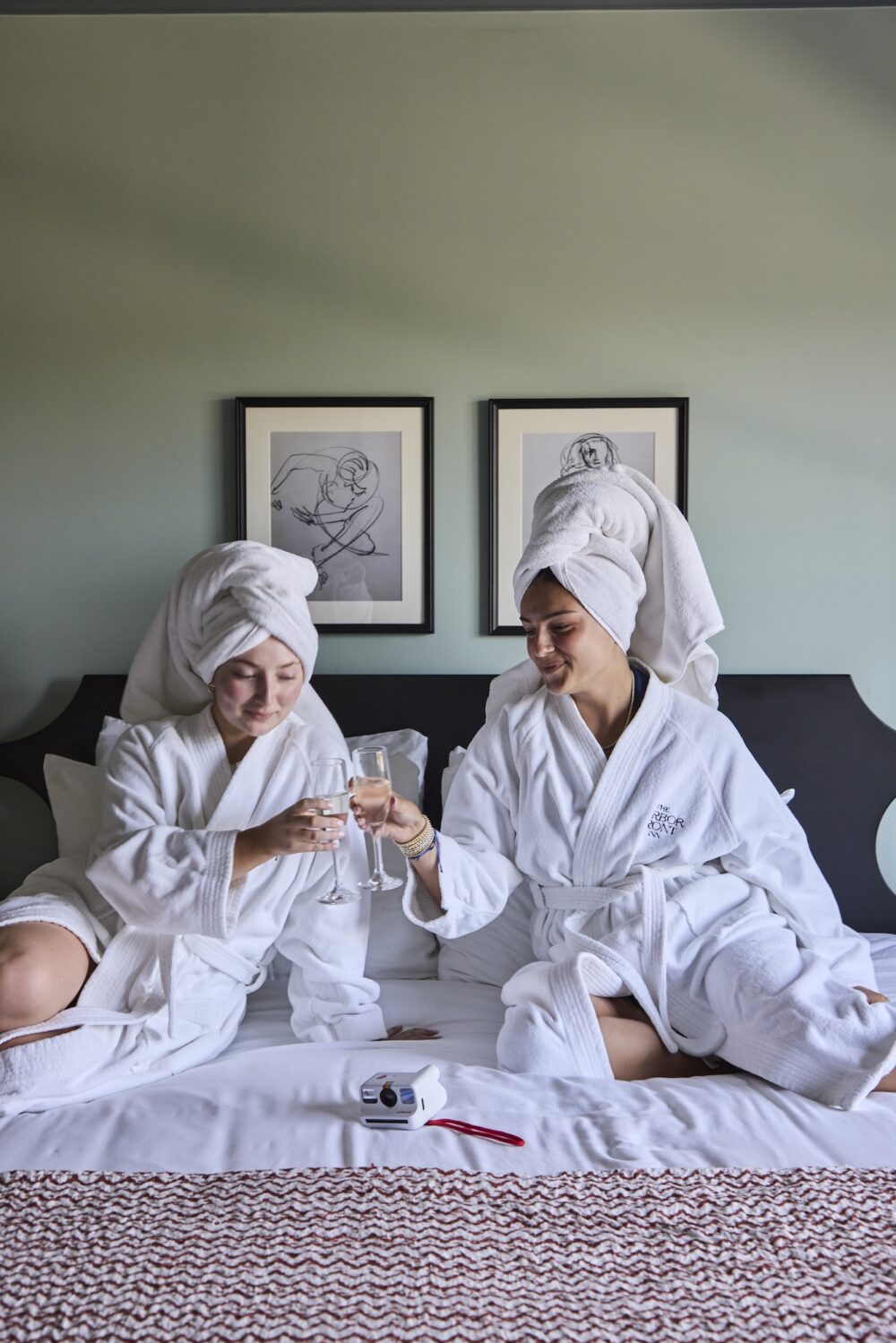 Two women in bathrobes toasting champagne in bed at The Harbor Front Inn.
